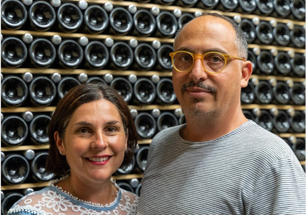 Two people smiling at camera with wall of stacked black speaker cones in background