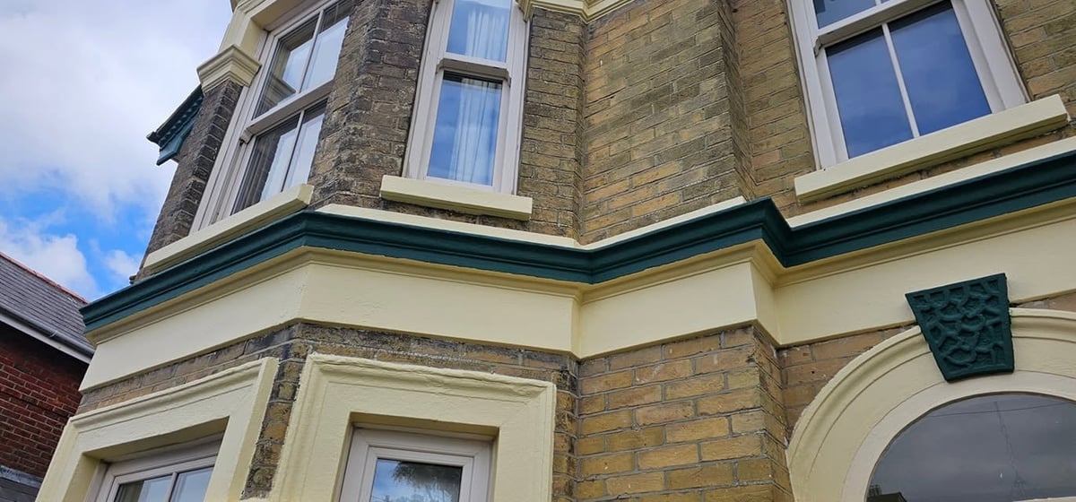 Historic Victorian building facade with cream and tan brick, mansard roof with dark green trim, and arched window detail