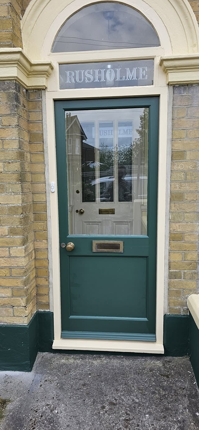 Green and white entrance door to Rusholme building with arched transom window and cream-colored surrounding frame