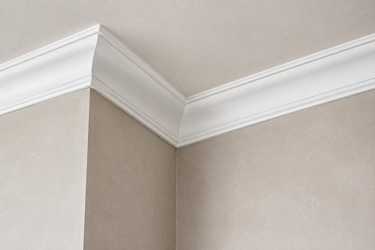 Close-up of white decorative crown molding where the ceiling meets the walls in a room with beige walls