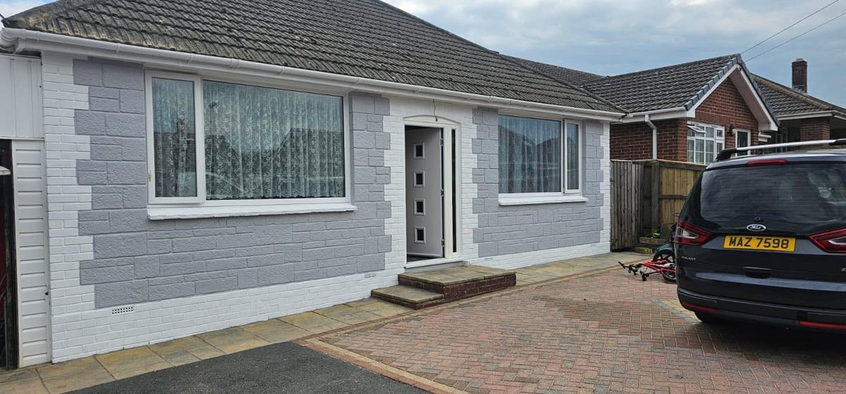 Modern single-story bungalow with white rendered walls, large windows, dark roof, brick driveway, and parked car
