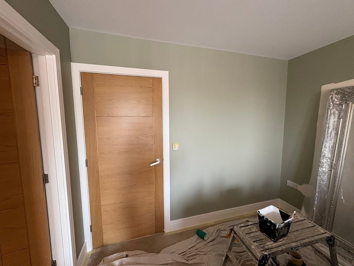 Interior room with sage green walls, wooden doors with white trim, paint supplies and equipment on floor during renovation