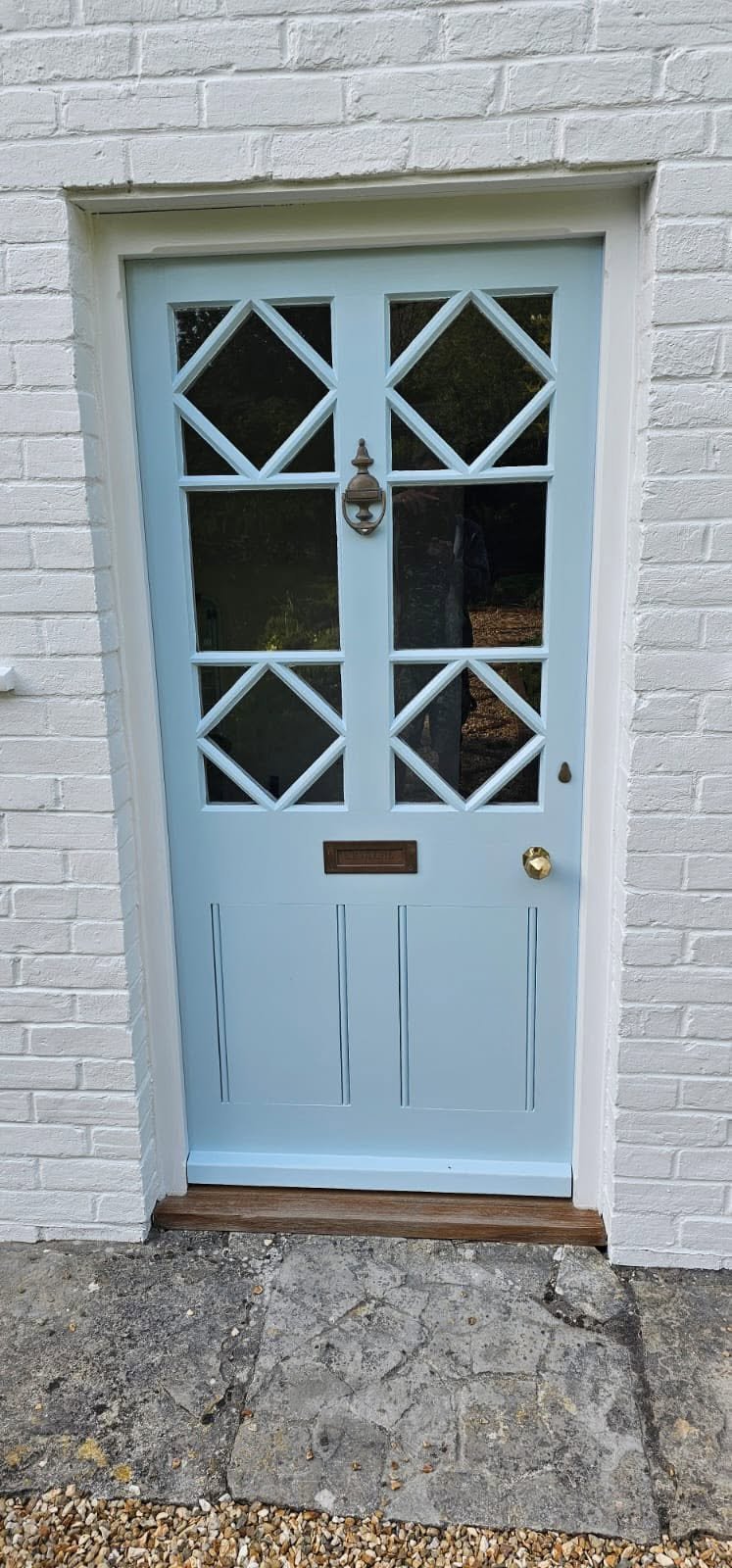Light blue front door with diamond-patterned window panes on a white brick house facade