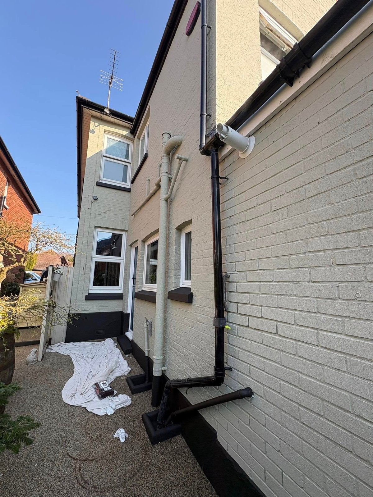 Modern terraced house with cream and gray brick exterior, black trim, featuring a downpipe and guttering system during construction or renovation