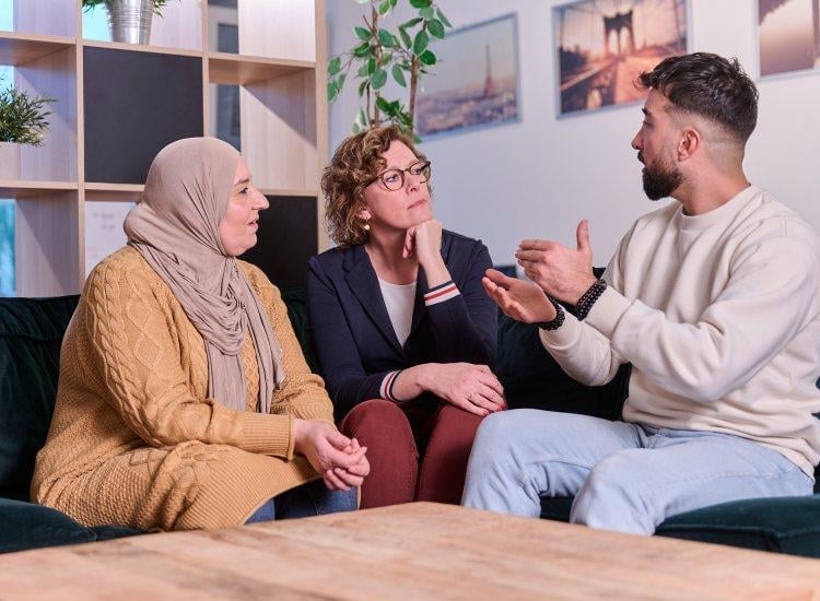 Three people having a conversation while sitting on a couch in a modern office or living room setting