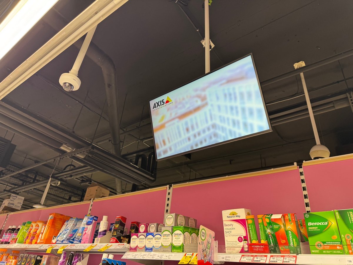 Ceiling-mounted commercial digital display screen above retail shelving in a Melbourne store