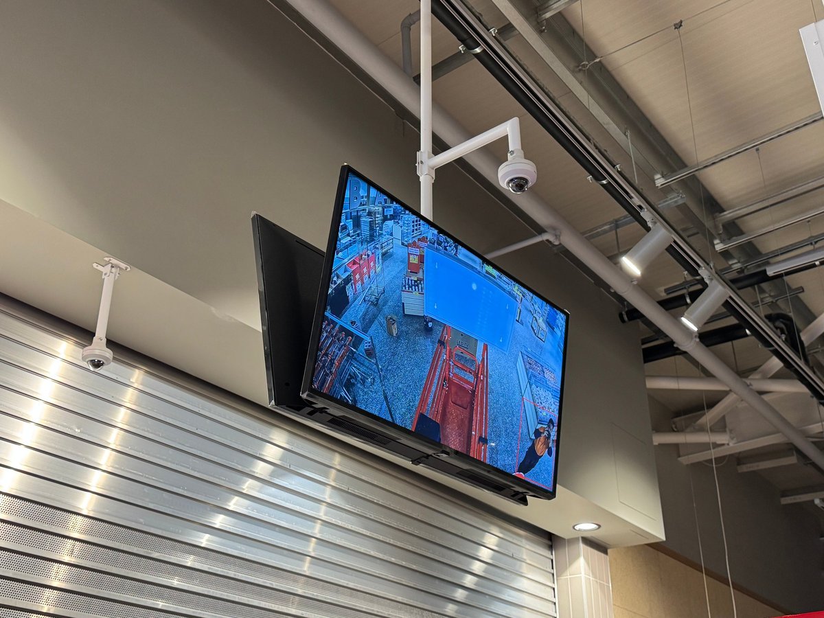 CCTV security camera system wall-mounted above a TV display in a modern Melbourne commercial interior with exposed ceiling fixtures