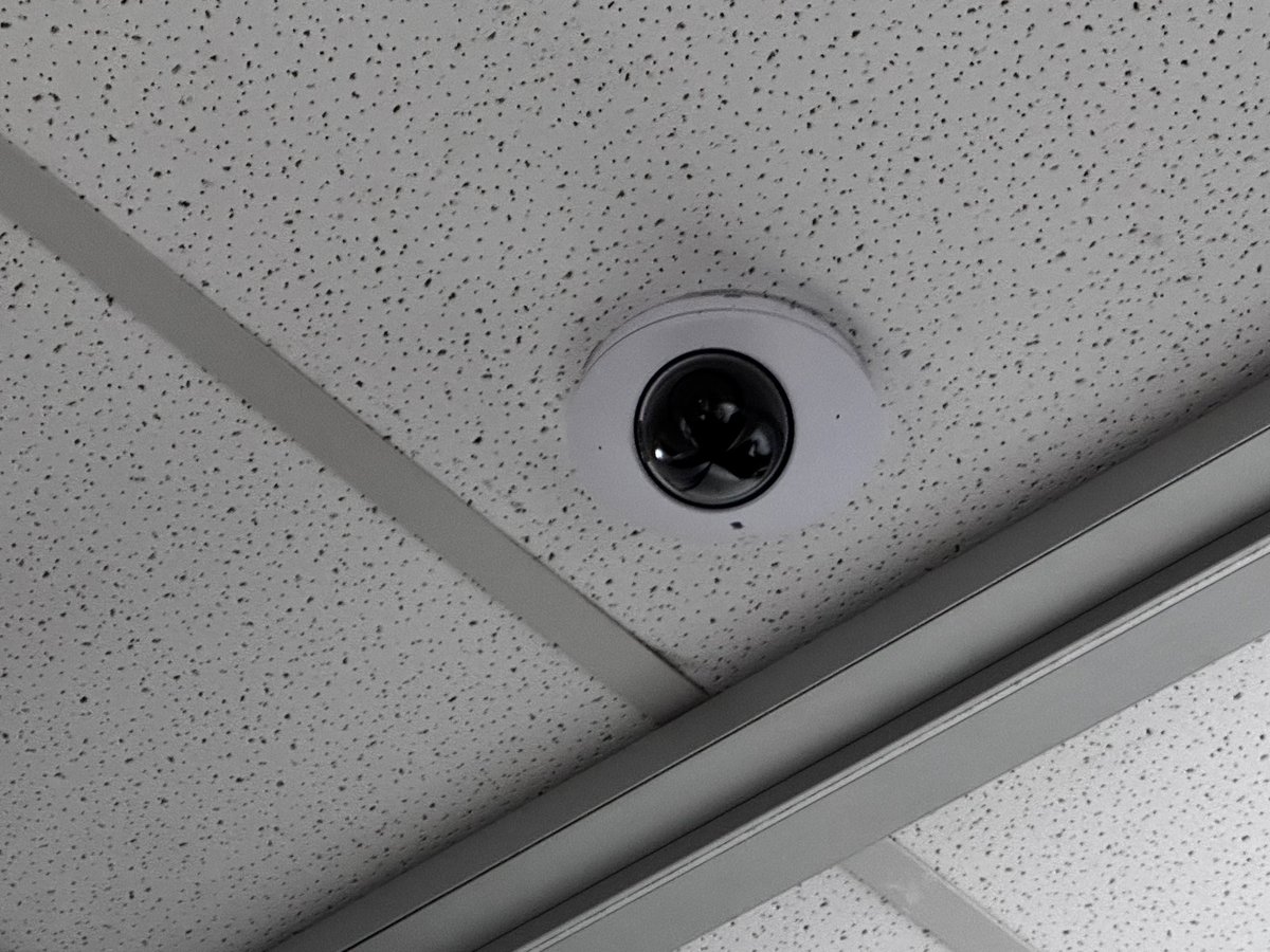 Ceiling-mounted black security camera dome on acoustic drop ceiling with metal trim at a commercial Melbourne site