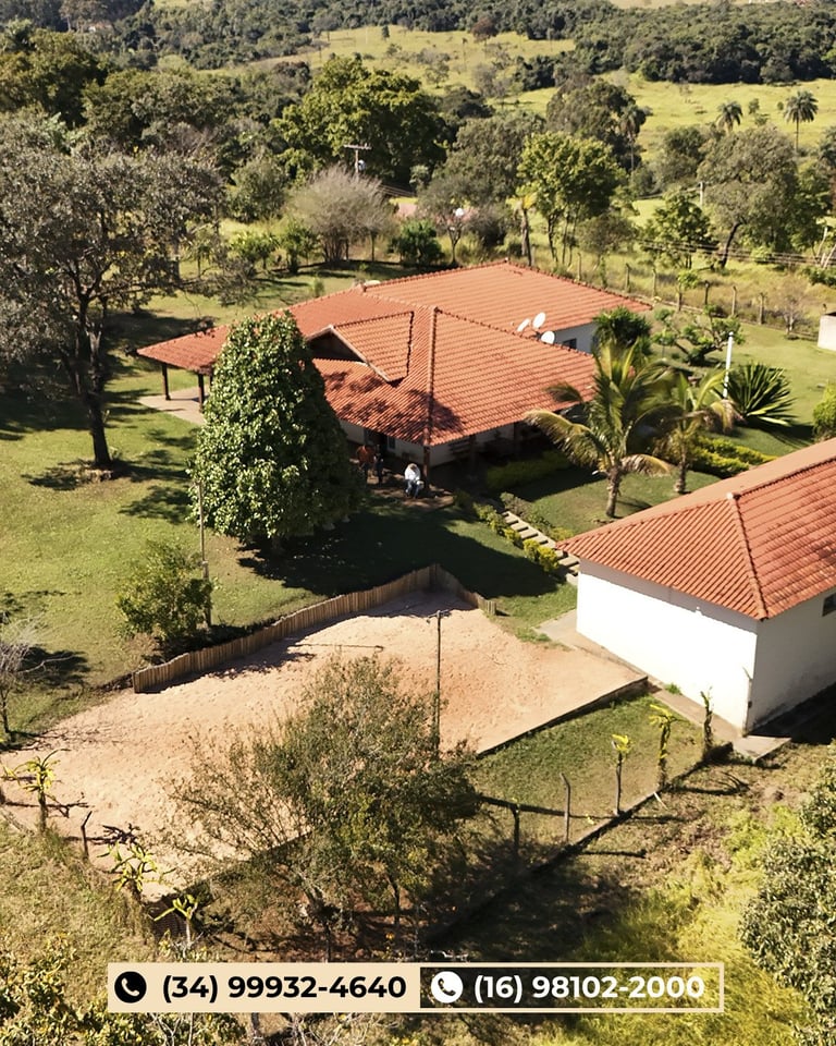 Vista aérea de propriedade com casas de telhado de barro, gramado, árvores dispersas e áreas cercadas entre colinas