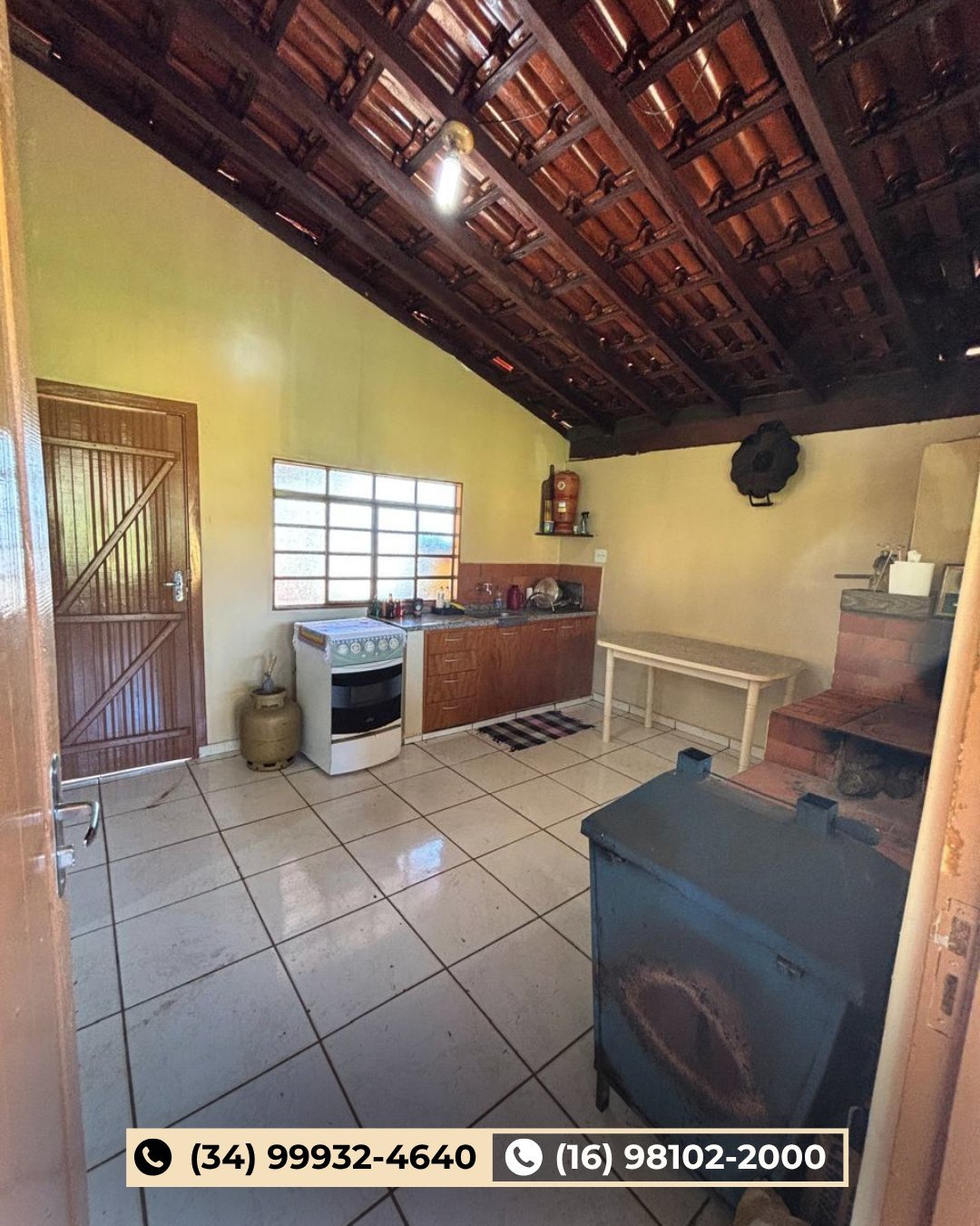 Cozinha rústica com paredes amarelas, piso de cerâmica, fogão branco, armários de madeira e teto com vigas aparentes