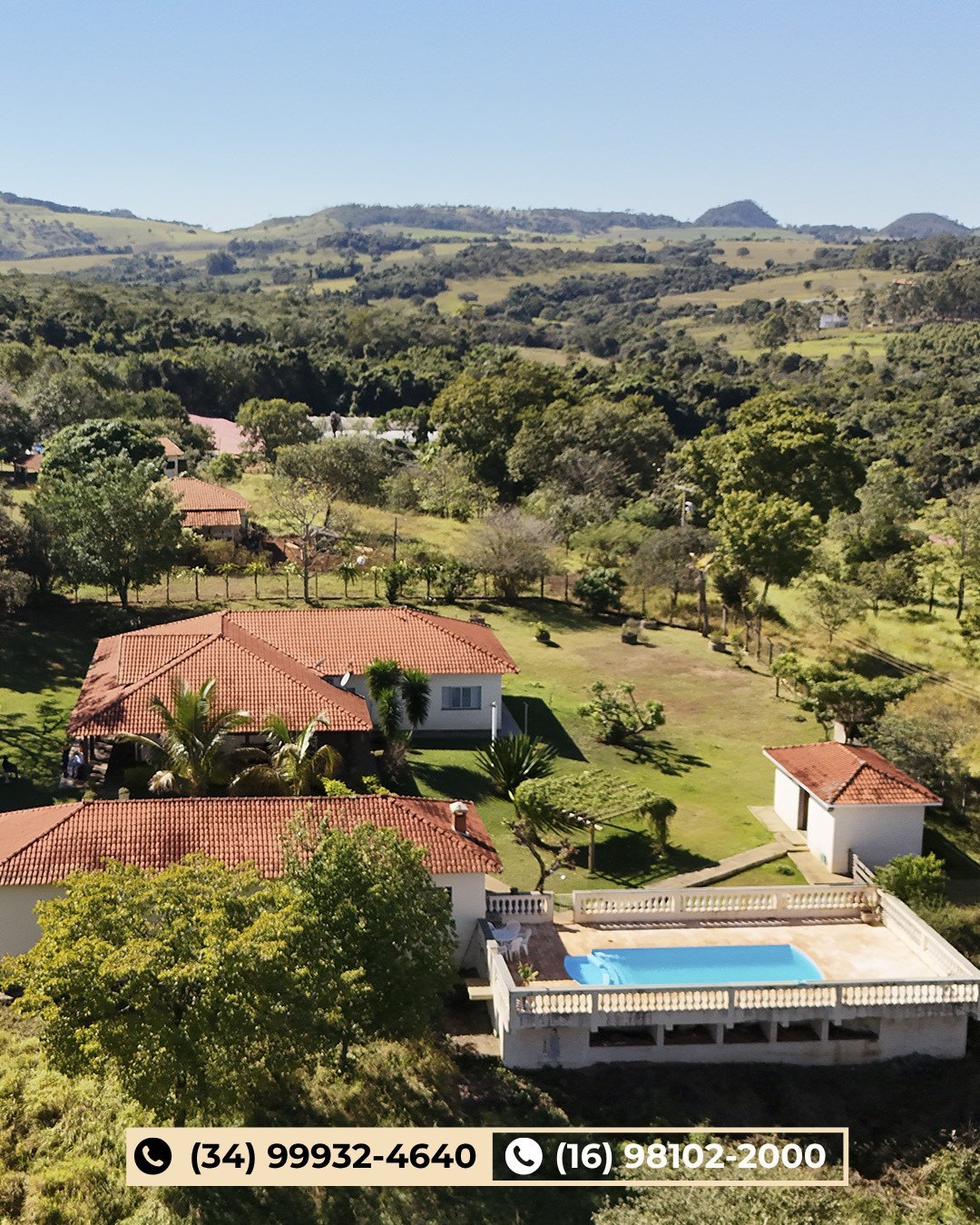 Vista aérea de propriedade rural com construções de telhado colonial, piscina e jardins verdes sobre colinas