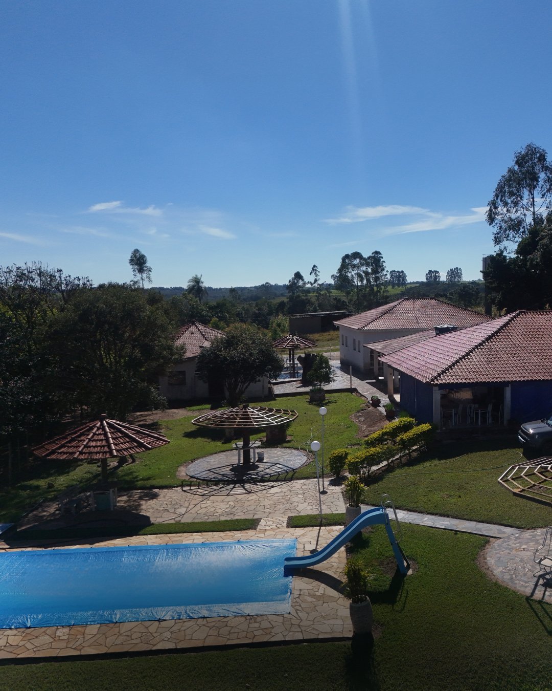 Vista aérea de propriedade residencial com piscina azul, gramado aparado, construções de telhado colonial e árvores ao redor