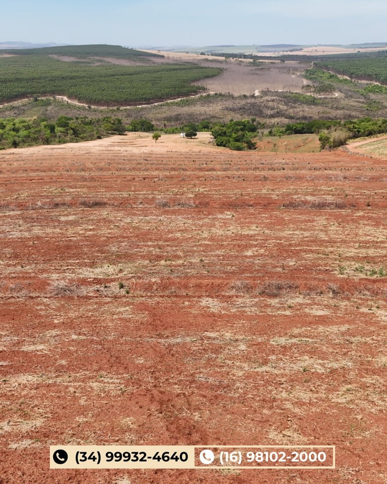 Vista aérea de área rural com solo vermelho em primeiro plano, campos agrícolas verdes e árvores ao fundo
