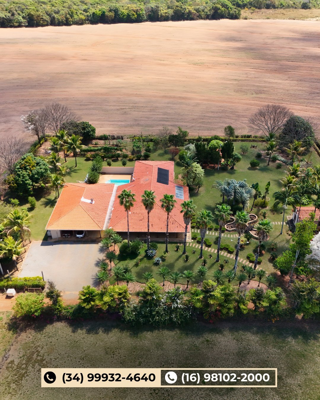 Vista aérea de grande sede com telhado vermelho, jardins cuidados, palmeiras, piscina e campos extensos ao redor