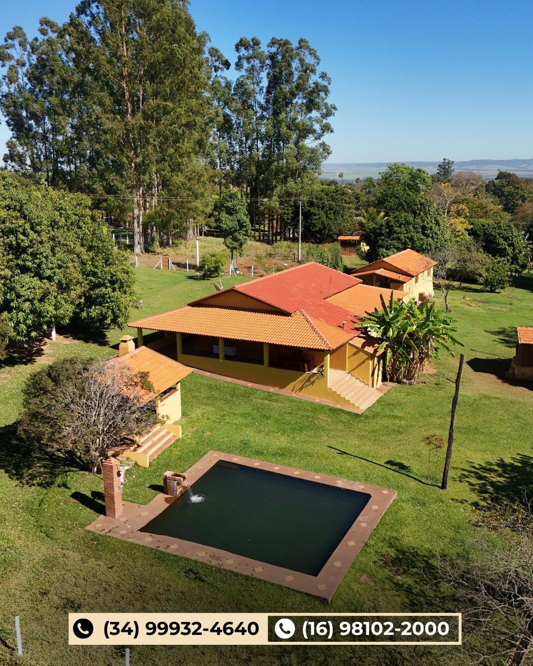 Vista aérea do sítio com casa sede de telhado colonial, piscina, gramado, eucaliptos e serra ao fundo