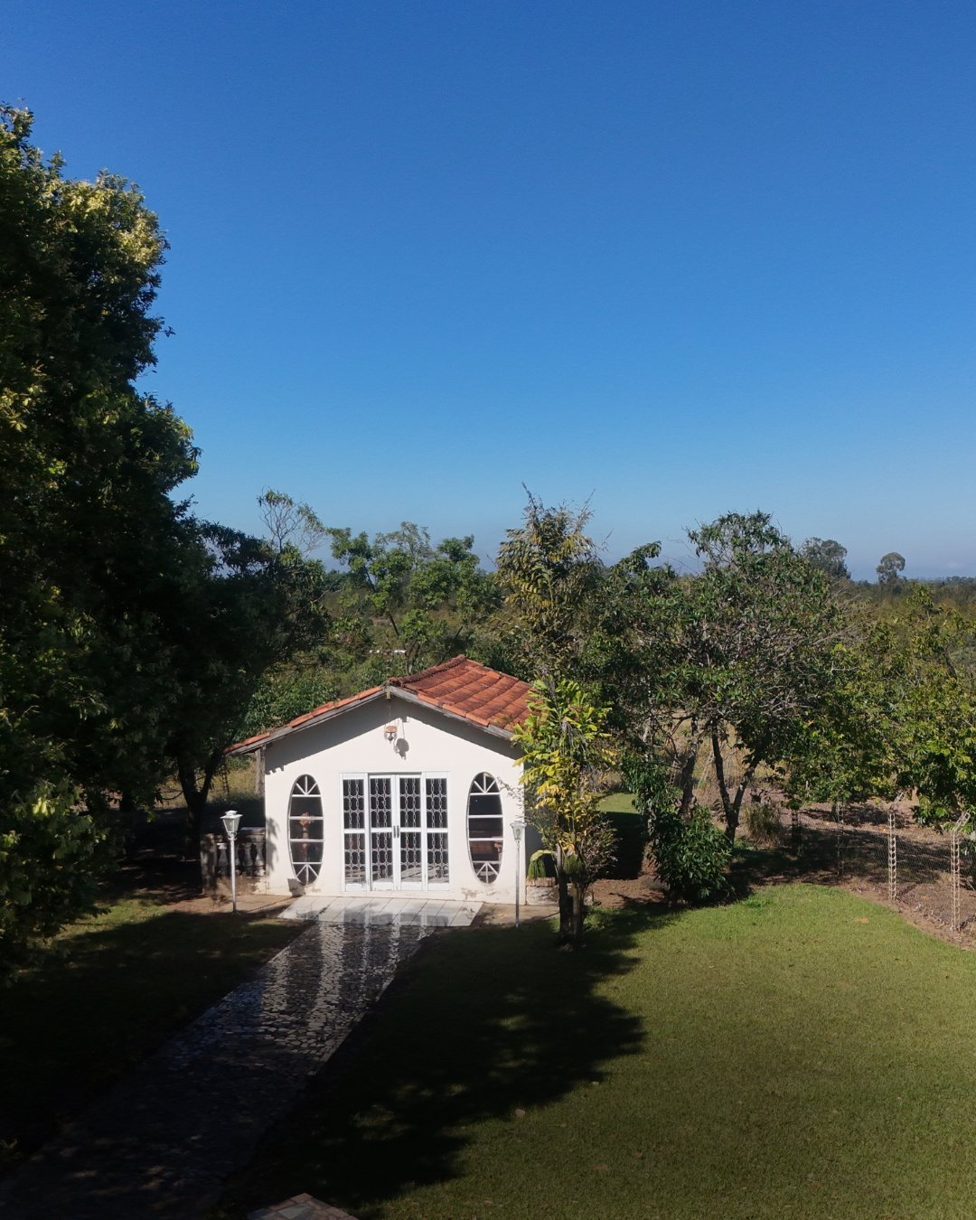 Casa branca de jardim com telhado vermelho cercada por árvores e gramado verde em ambiente rural