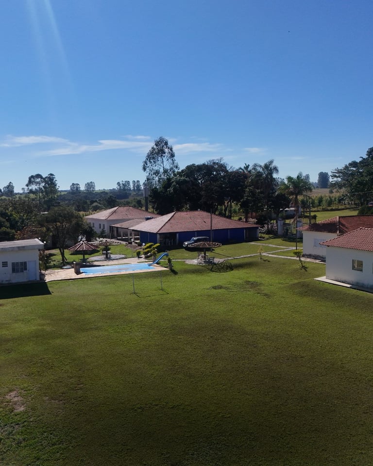 Vista aérea de sede rural com casa principal de telhado colonial, piscina, casas de hóspedes e jardins cercados por árvores