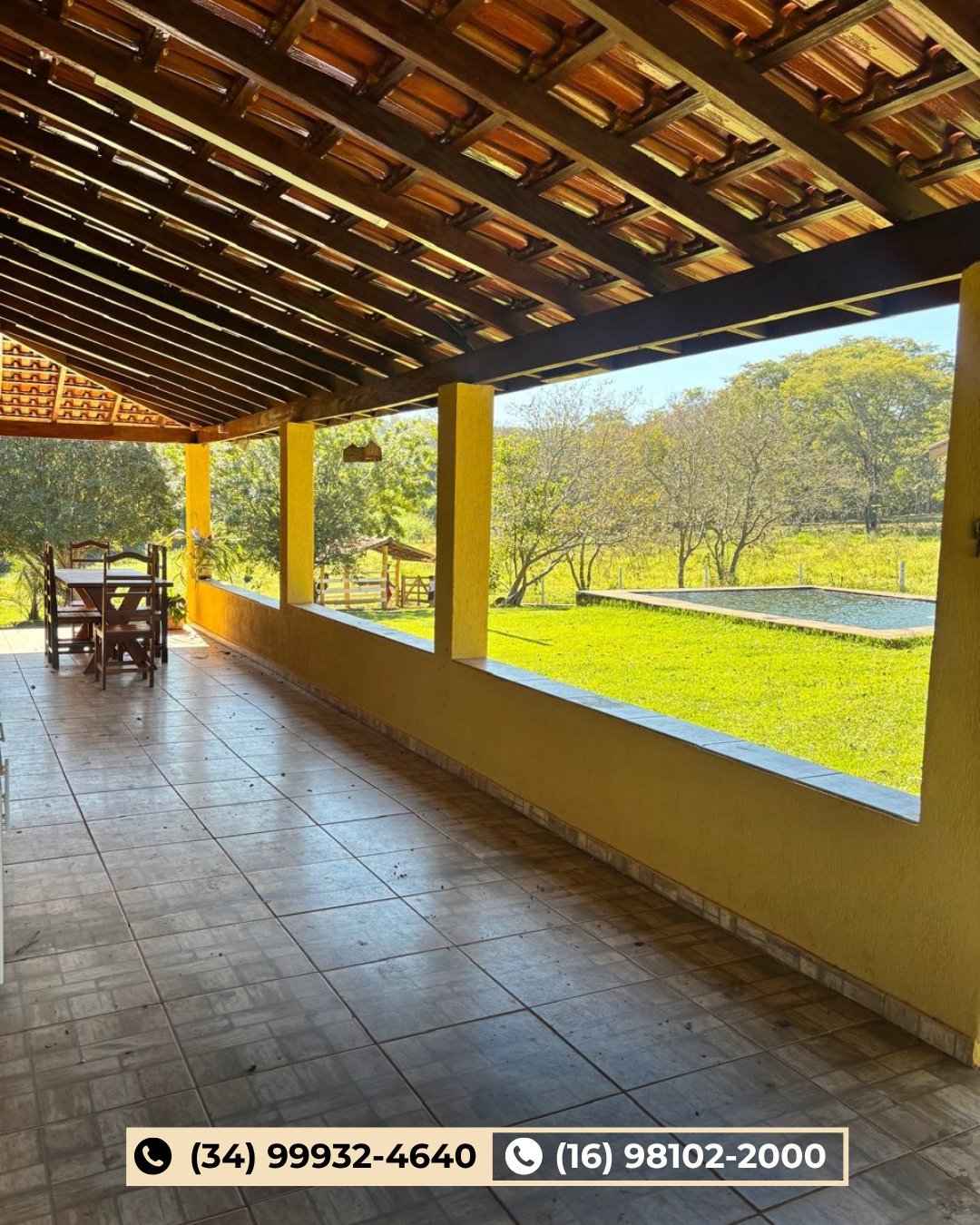Varanda coberta do sítio com piso de cerâmica, vigas de madeira e vista para o gramado e árvores