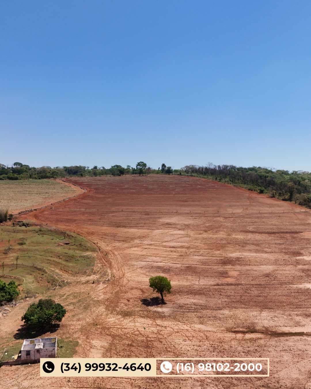 Grande área agrícola de solo vermelho limpo com vegetação esparsa e morros ao fundo
