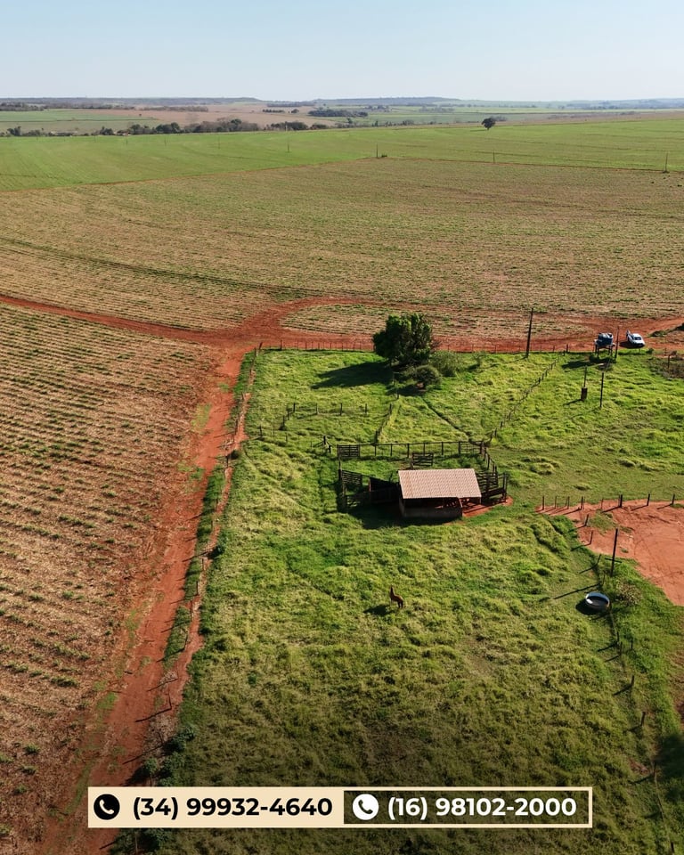 Vista aérea de propriedade rural com solo vermelho, pastagem verde, construções e curral