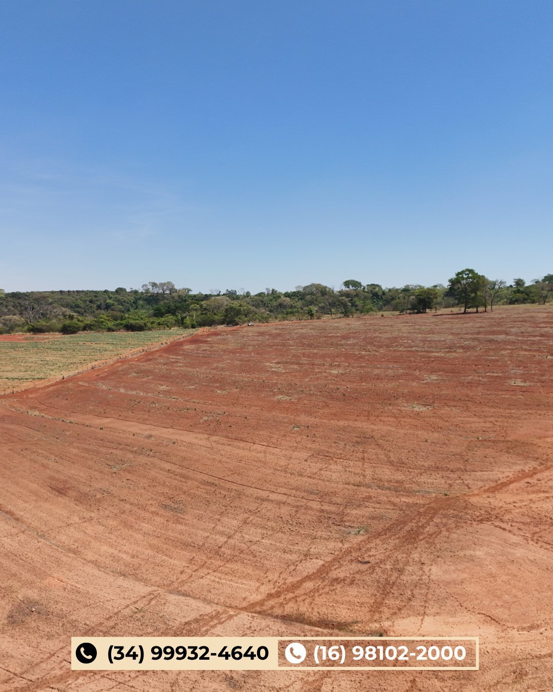 Vista aérea de grande campo de solo vermelho arado sob céu azul com árvores ao fundo
