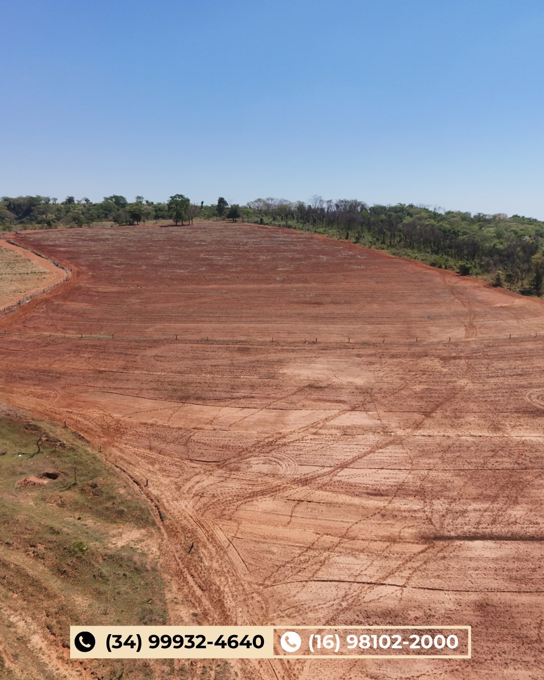 Grande área de solo vermelho limpo com morros florestados ao fundo sob céu azul