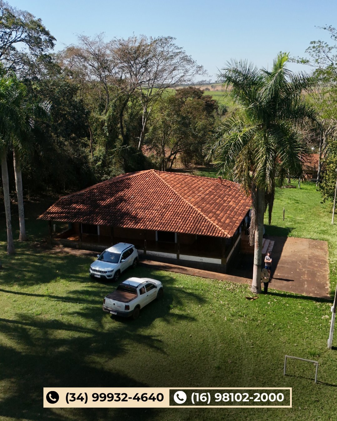 Vista aérea de garagem coberta de telhado colonial com dois carros brancos, gramado e palmeiras