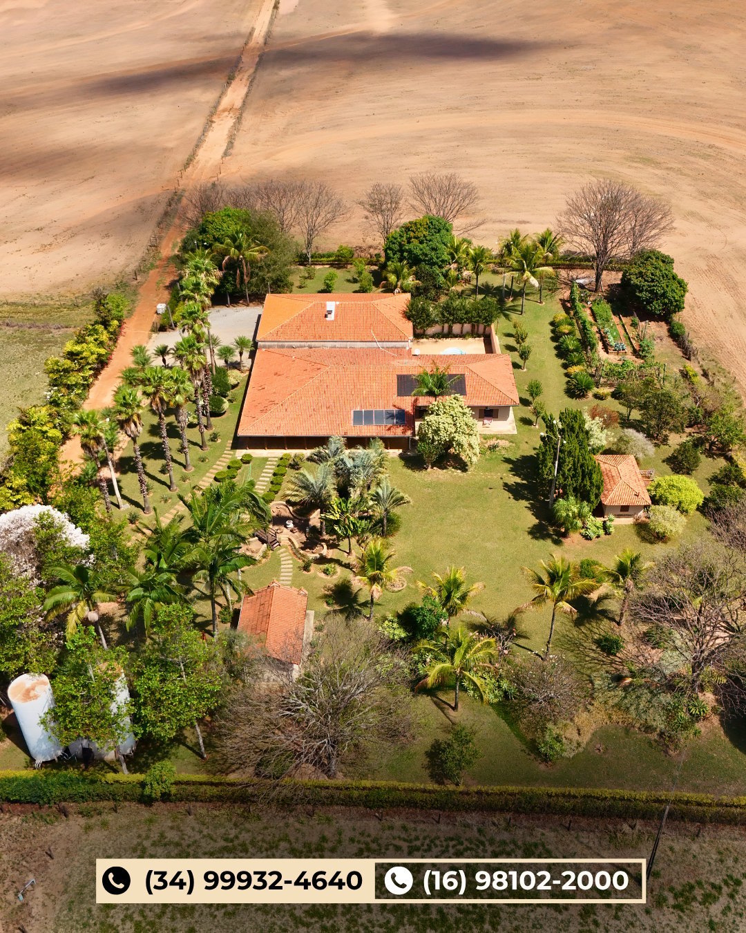 Vista aérea de propriedade rural com telhado colonial, painéis solares, jardins cuidados e lavouras ao redor
