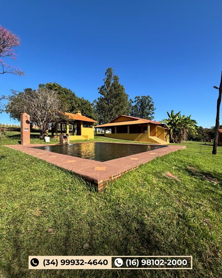 Casa amarela rural com telhado de barro e espelho d'água em paisagem gramada sob céu azul
