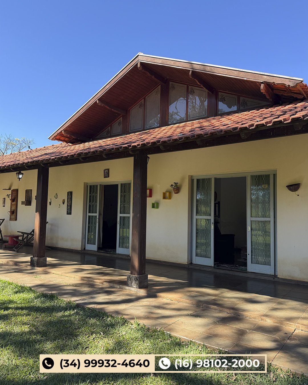 Casa térrea moderna com paredes creme, telhado escuro, varanda coberta e grandes portas de vidro sob céu azul