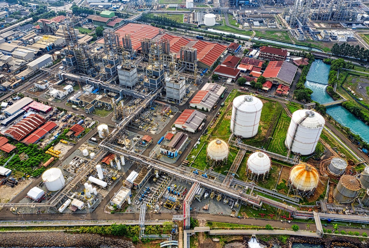 Aerial view of an industrial complex with storage tanks, chemical plants, and refinery facilities along a waterway.