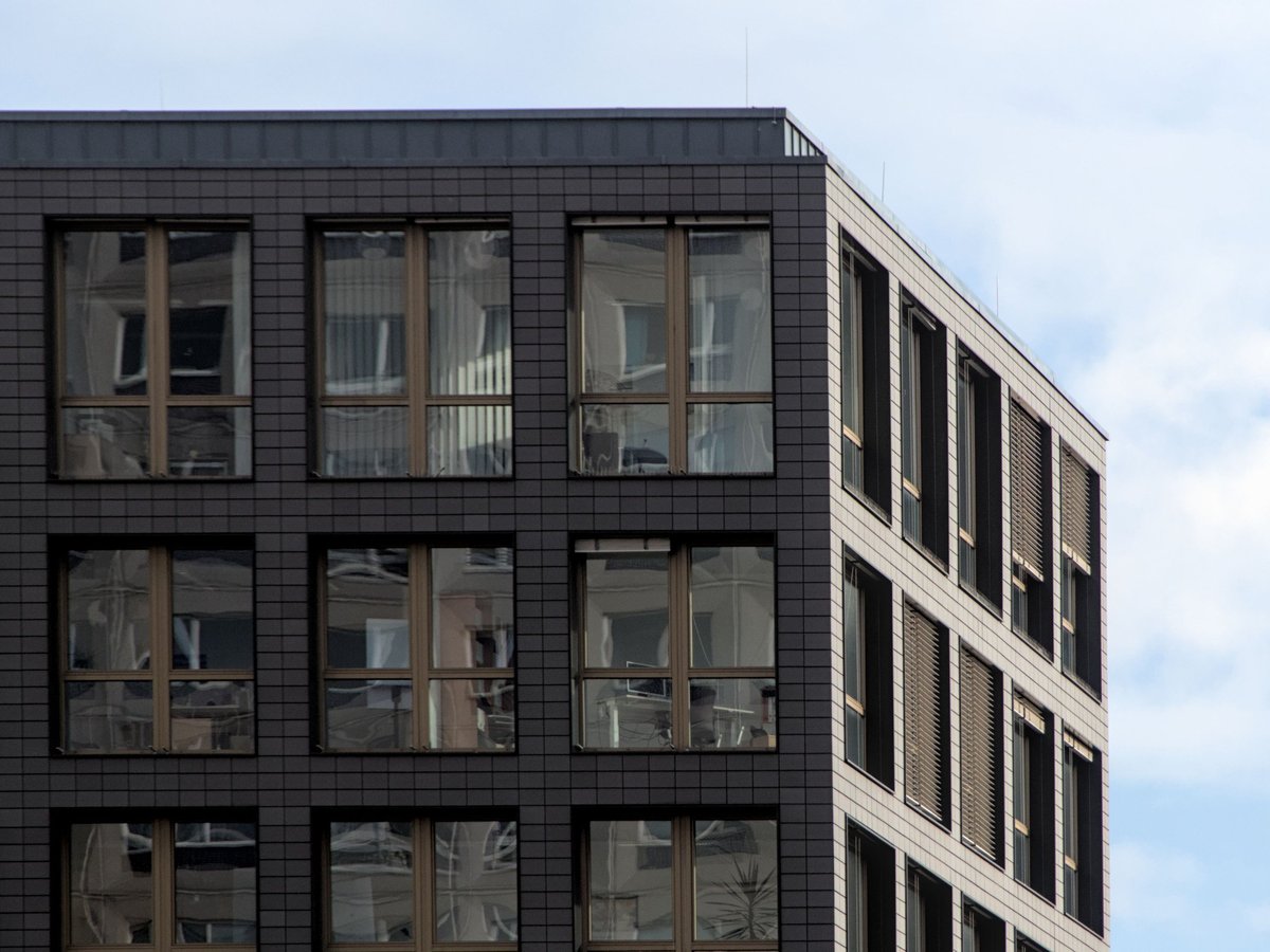Modern black residential building with large grid-patterned windows against a cloudy sky