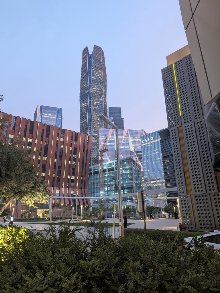 Modern urban plaza at dusk with tall skyscrapers, a distinctive twisted tower, landscaping, and illuminated buildings in a downtown cityscape