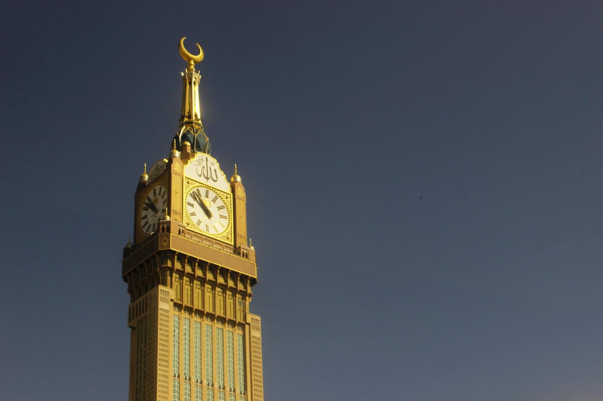 Golden clock tower with Islamic crescent finial against a blue sky