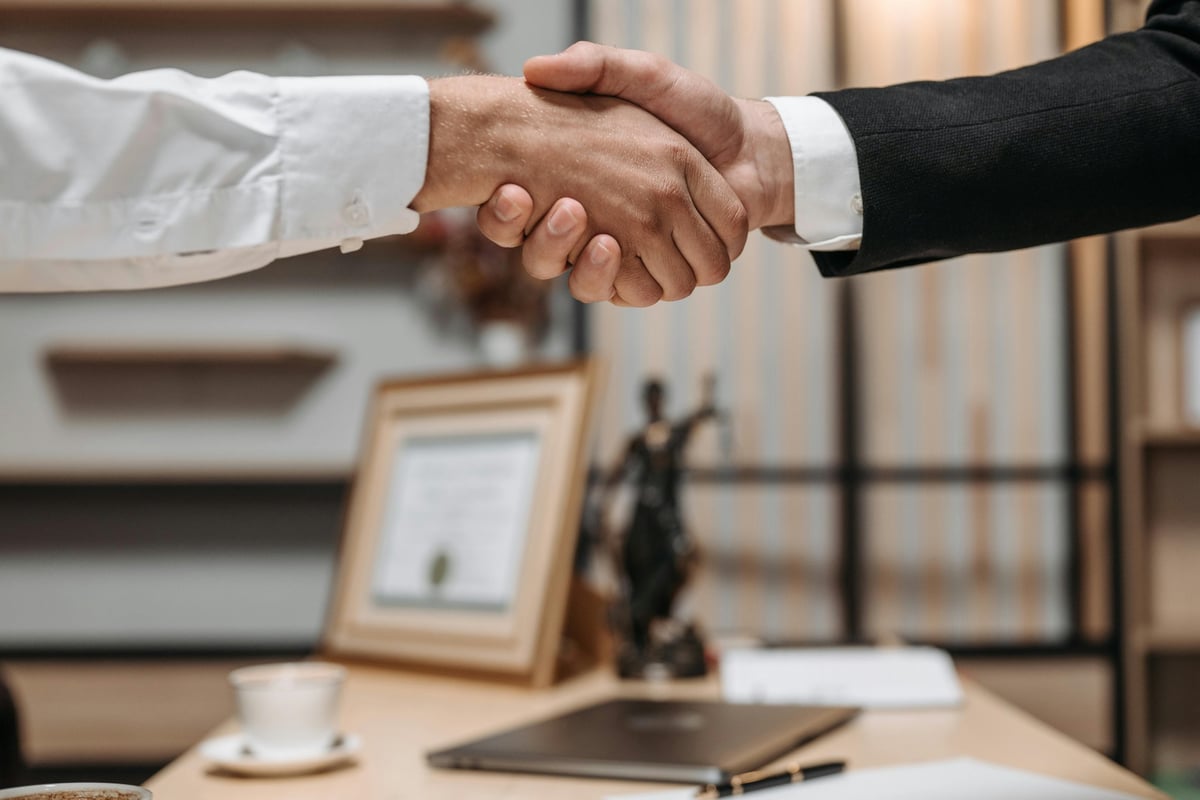 Two businesspeople shaking hands in a professional office setting during a business meeting or deal agreement.