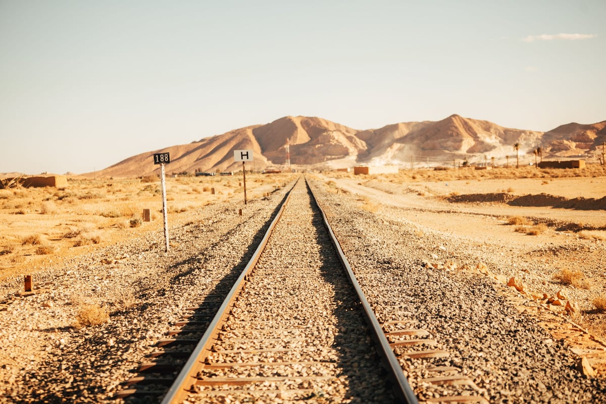 Railway tracks stretching through a desert landscape with rocky mountains in the distance