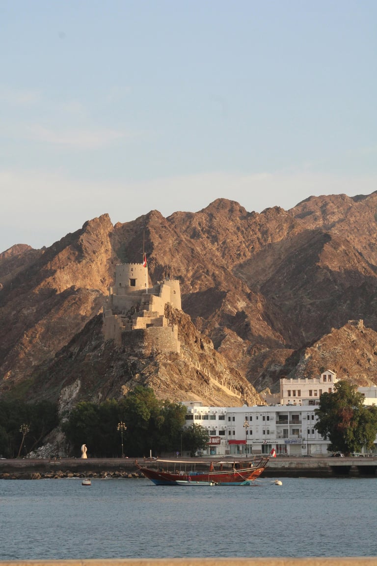 Ancient fort on rocky mountain overlooking river with traditional wooden boat and white building in foreground