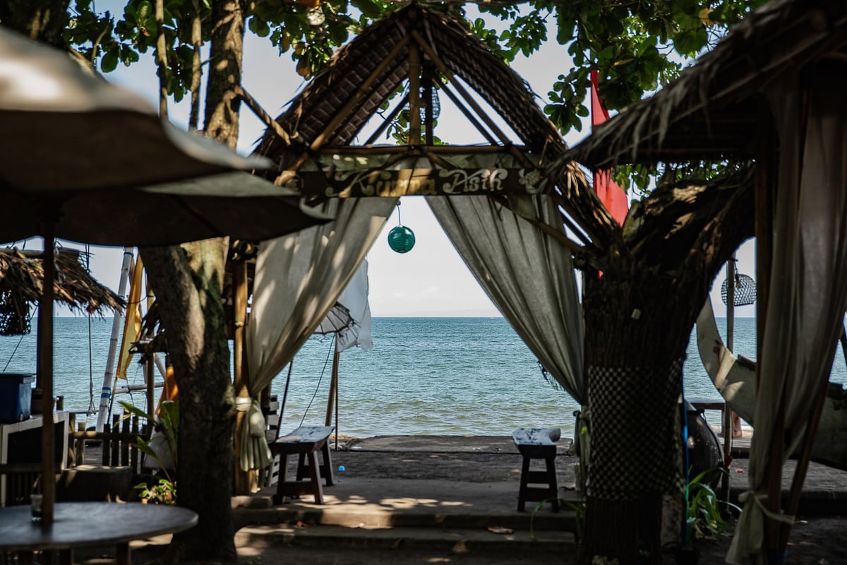Beachfront gazebo with sheer curtains framing a view of the ocean and sandy beach.