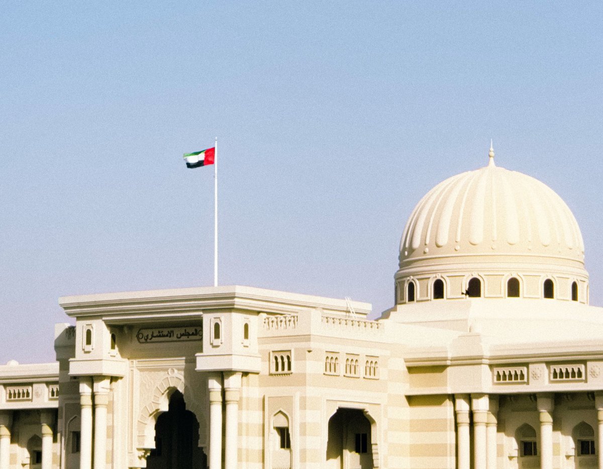Cream and beige government building with a large domed roof and Kuwaiti flag on a white pole against a clear blue sky