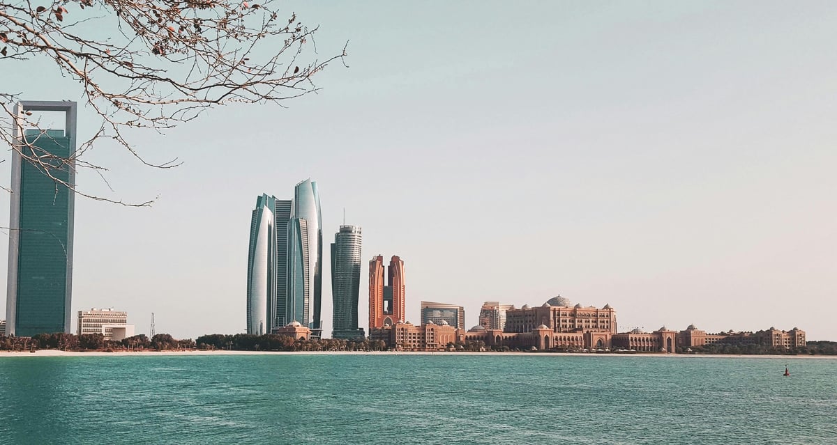 Skyline of Abu Dhabi with modern high-rise buildings reflected in turquoise water under clear sky