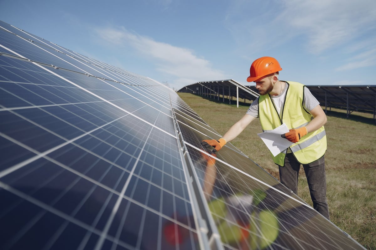 Worker in safety gear cleaning solar panels in a field under blue sky