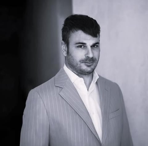 Professional headshot of a man in a pinstriped gray suit and white shirt against a plain background