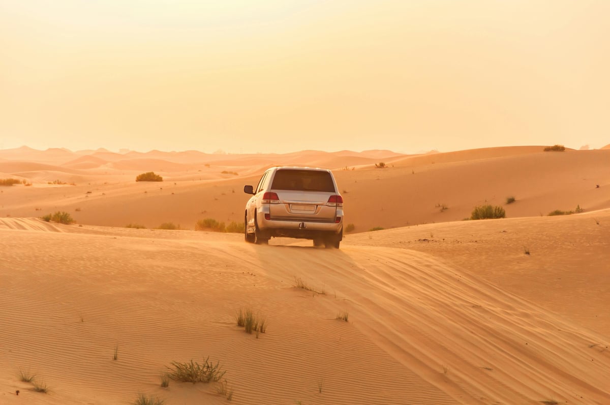 SUV driving through vast sand dunes in desert landscape with sparse vegetation