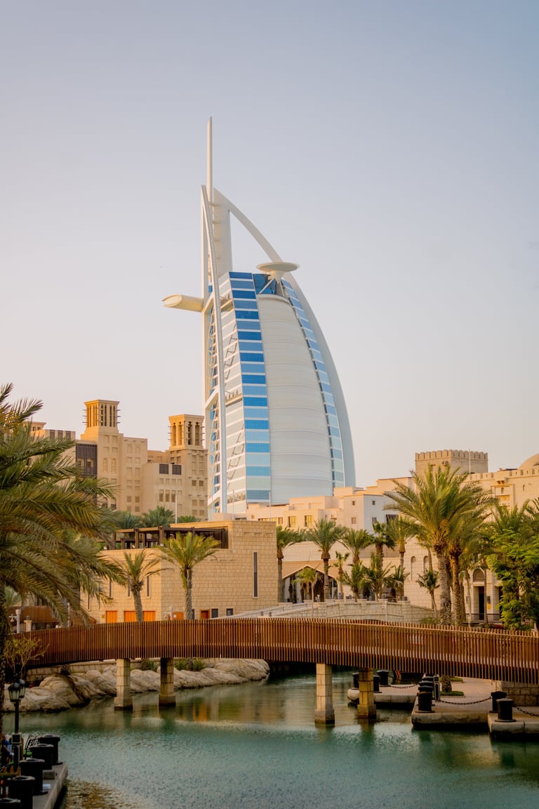 Burj Al Arab luxury hotel in Dubai with distinctive sail-shaped architecture, palm trees, and waterfront canal with boats