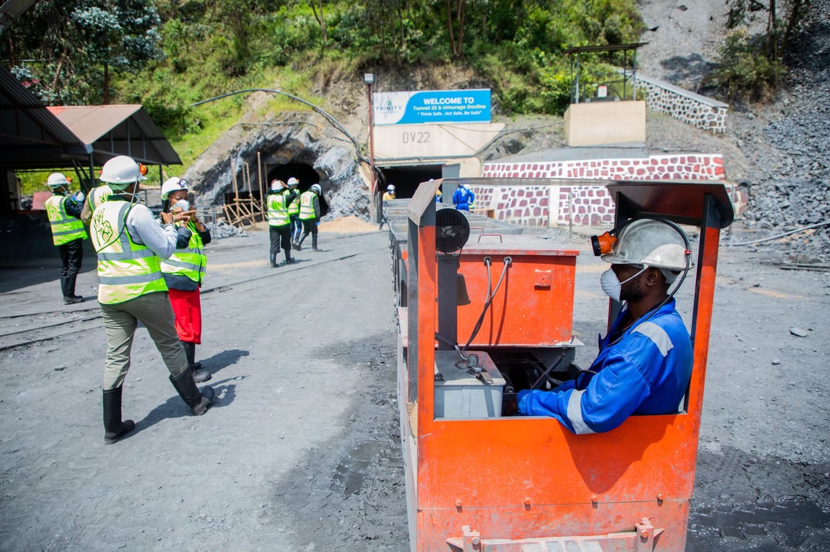 Construction site with workers in safety gear operating an orange elevated platform and heavy machinery near a mountain entrance.
