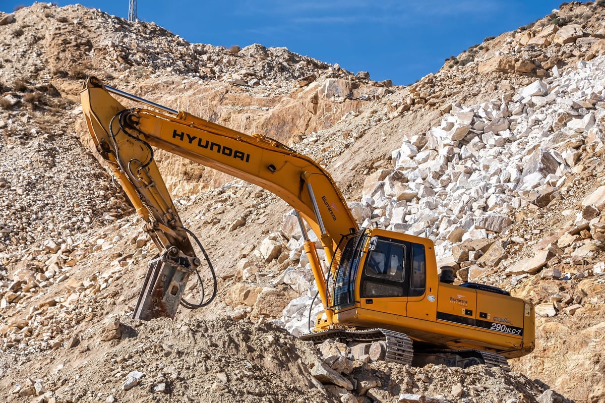 Yellow Hyundai excavator with extended boom working in rocky stone quarry against clear blue sky