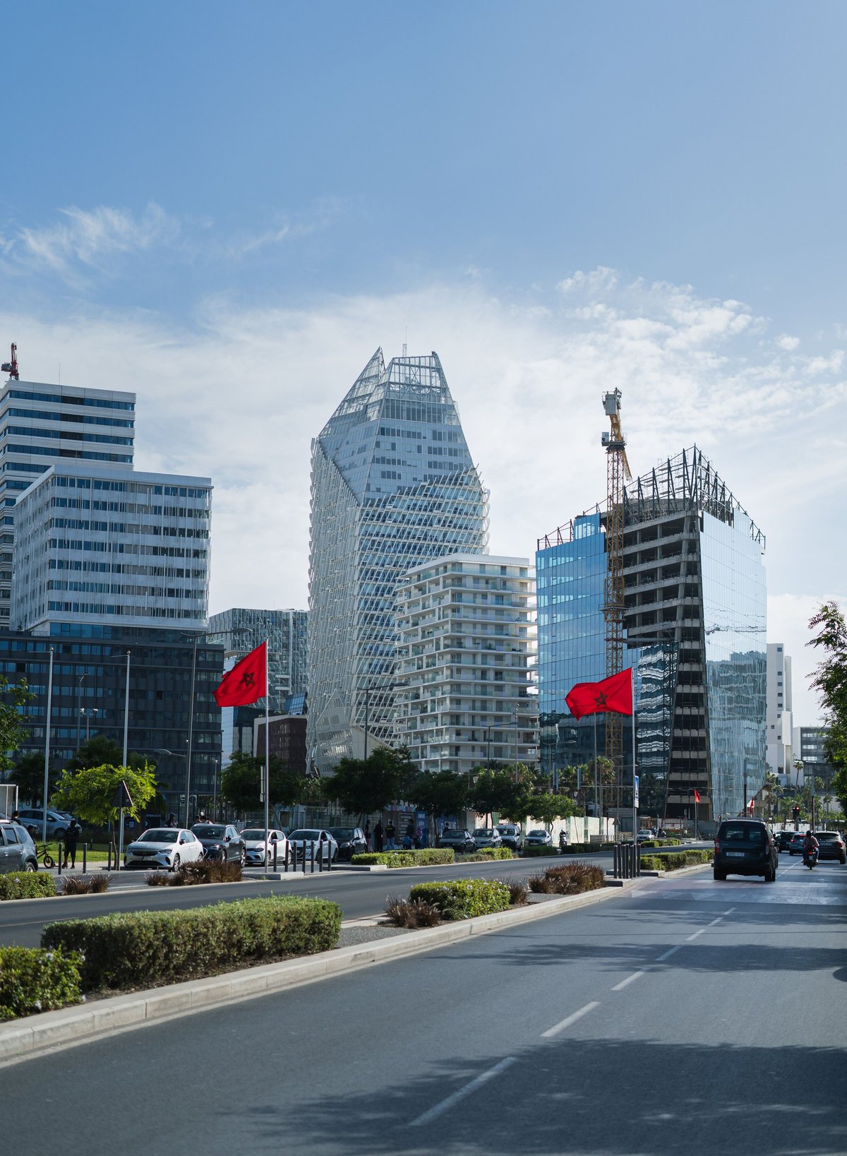 Urban street with modern high-rise buildings and red flags under blue sky with clouds