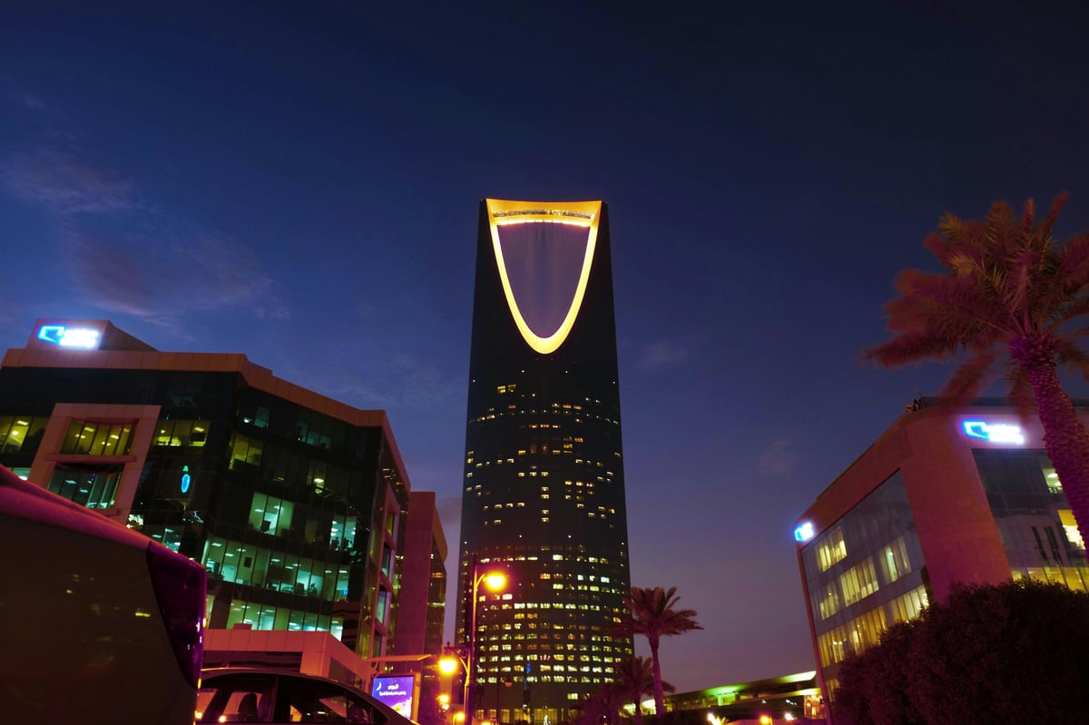 Illuminated skyscraper with distinctive curved top at dusk in modern cityscape with surrounding buildings and palm trees