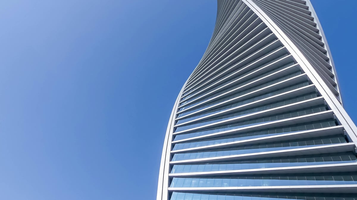 Curved modern skyscraper with horizontal glass and steel bands photographed from below against a clear blue sky