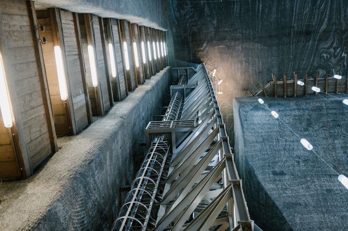 Industrial metal stairs descending into a concrete basement or storage area with metal doors and shelving visible